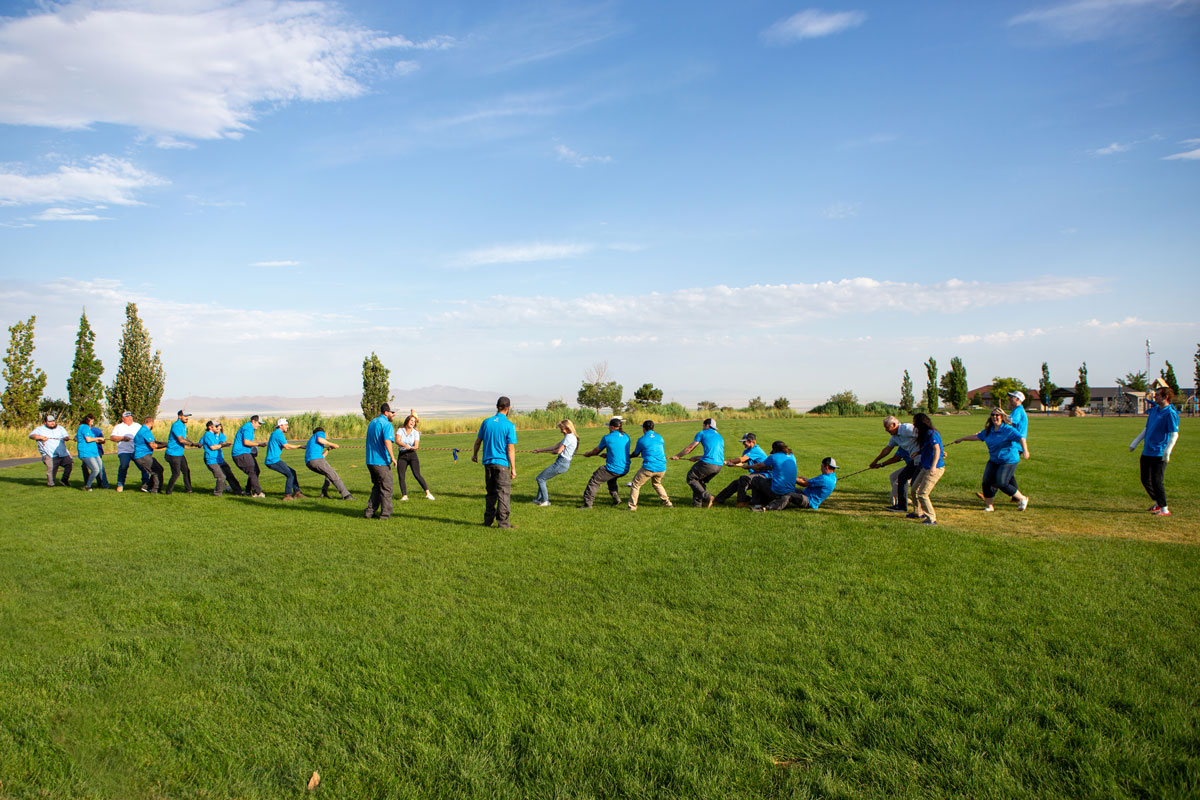 Blue Best team playing tug of war in grassy field with bright blue sky